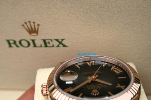 IMG_7151 | SD Watches Close-up of a rose-gold Rolex wristwatch on a white cushion, with a beige wall featuring the Rolex crown logo in the background.