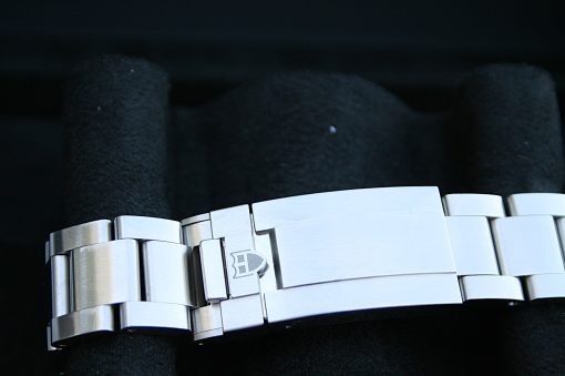 IMG_7196 | SD Watches Close-up of a stainless steel bracelet with interlocking links on a dark surface, showing a small logo on the clasp edge.