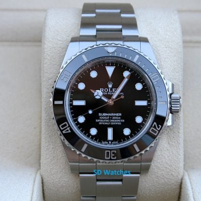 Rolex 124060 | SD Watches Close-up of a stainless steel Rolex Submariner watch on a beige display cushion, featuring a black dial and silver bezel edge accessibly visible in front of the camera.