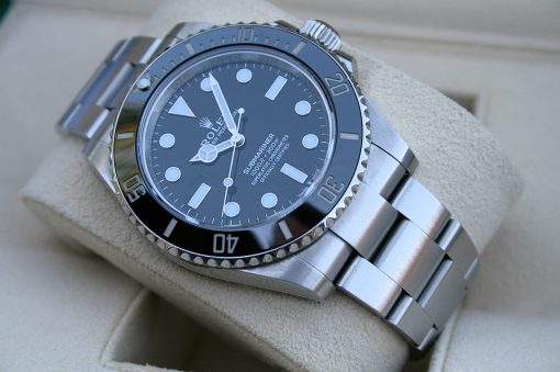 IMG_7249 | SD Watches Close-up of a stainless steel Rolex Submariner on a beige cushion, showing a black dial with luminous markers and a unidirectional bezel.