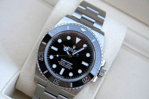 IMG_7261 | SD Watches Close-up of a stainless steel Rolex Submariner watch with a black dial and silver bezel resting on a light cushion.