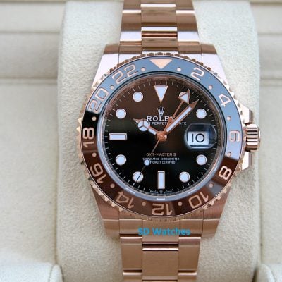 Rose gold Rolex GMT-Master II wristwatch on a beige display cushion, showing a black dial and date window at 3 o'clock.