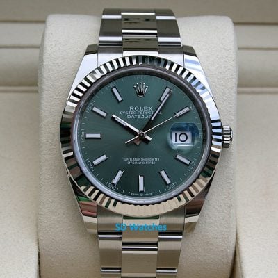Rolex Oyster Perpetual Datejust with green dial and fluted bezel on a beige display cushion, stainless steel bracelet