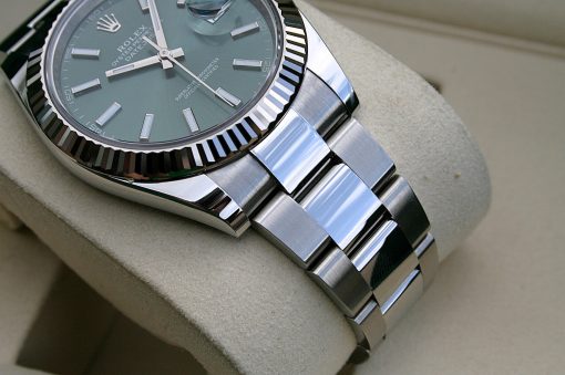 IMG_7287 | SD Watches Close-up of a Rolex watch with a fluted bezel, green dial, and brushed steel bracelet on a beige cushion