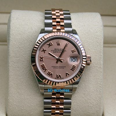 Two-tone Rolex Datejust wristwatch with pink dial, Roman numeral hour markers, and a date window on a beige display cushion.