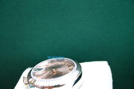 IMG_7306 | SD Watches Close-up of a gold-tone wristwatch resting on a white cushion with a dark green background behind it.