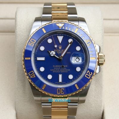 Close-up of a two-tone Rolex Submariner watch with a blue dial and gold bezel on a beige cushion.