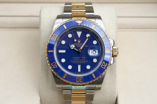 Rolex 116613 | SD Watches Close-up of a two-tone Rolex Submariner watch with a blue dial and gold bezel on a beige cushion.