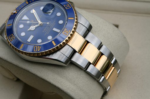 IMG_7341 | SD Watches Close-up of a blue-bezel Rolex Submariner with a two-tone gold and steel bracelet on a soft display cushion.