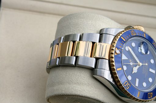 IMG_7342 | SD Watches Close-up of a two-tone Rolex watch with a blue bezel and steel-gold bracelet on a gray cushion.