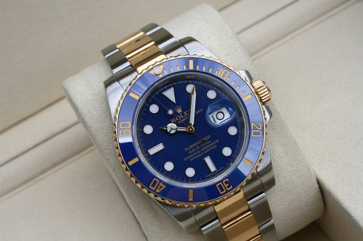 IMG_7350 | SD Watches Close-up of a two-tone Rolex Submariner watch with a blue dial and gold bezel resting on a light cushion.
