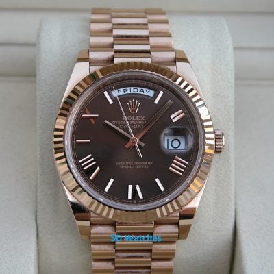 Rose gold Rolex Day-Date watch on a padded display cushion with day and date windows visible (Friday, 10).