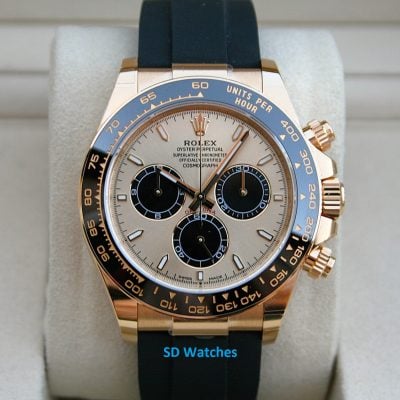 Close-up of a gold Rolex Daytona watch with a blue bezel on a light display cushion with a black strap.