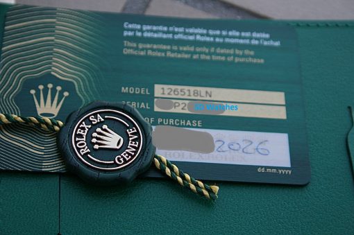 IMG_7400 | SD Watches Close-up of a teal Rolex warranty card with model and serial fields, featuring a black Rolex Geneva badge and green-gold rope in the foreground.