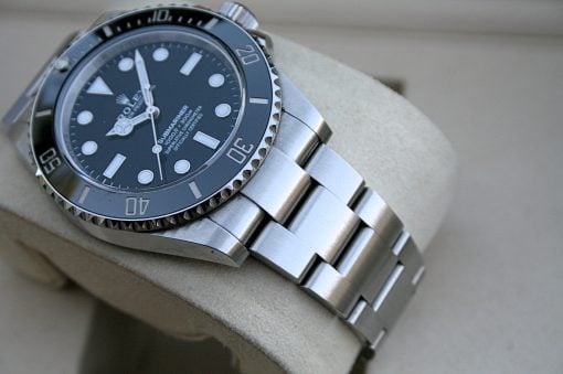 IMG_7434 | SD Watches Close-up of a stainless steel Rolex Submariner watch on a beige cushion, showing black dial and rotating bezel.